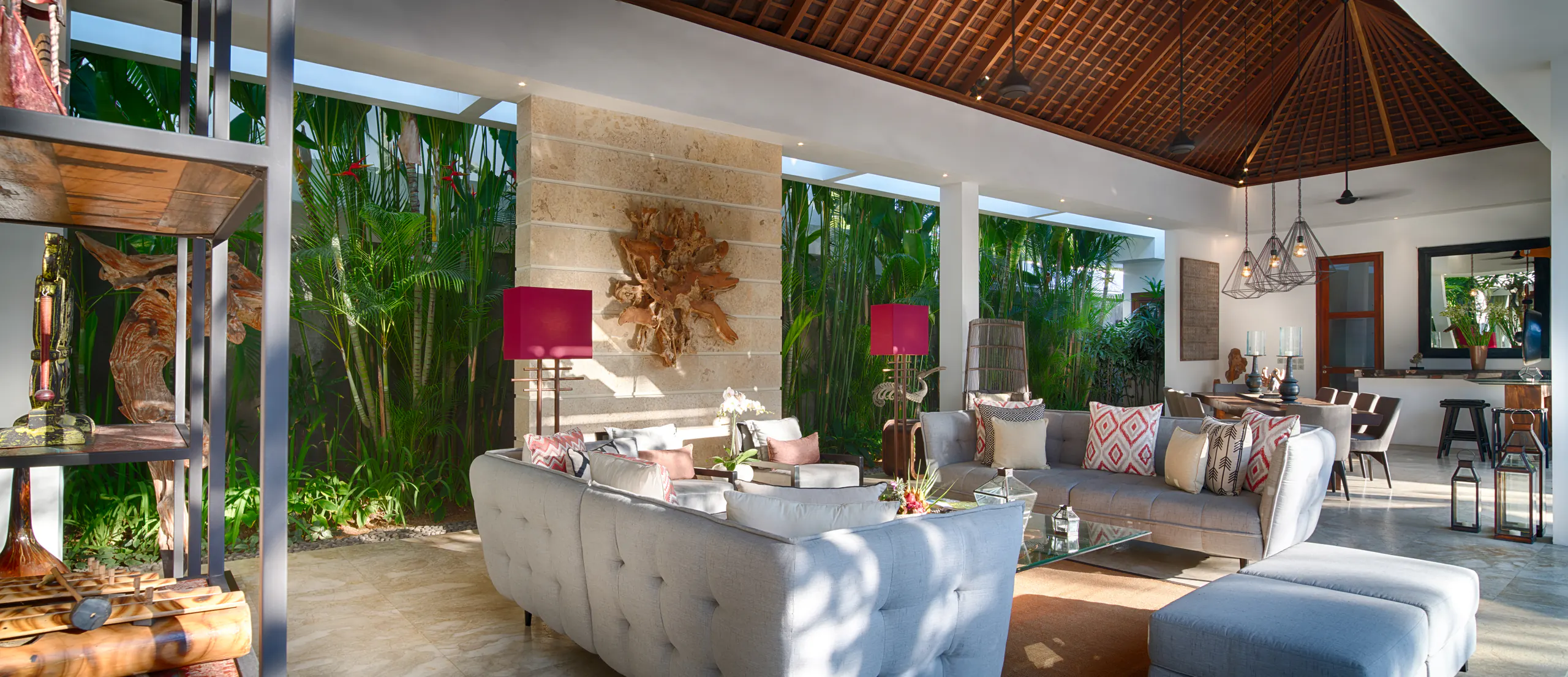 The living pavilion at Casa Brio, tufted sofas and claret lamps against a planted wall with the dining end beyond