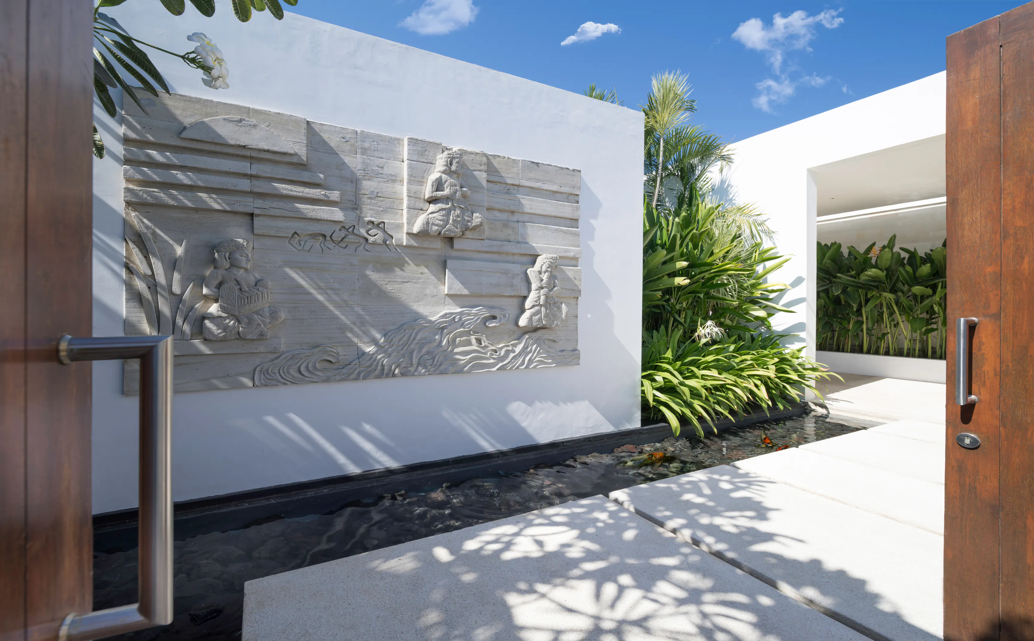 The entrance courtyard at Casa Brio, the timber doors standing open on a carved sandstone relief and the paved walk crossing the water to the house