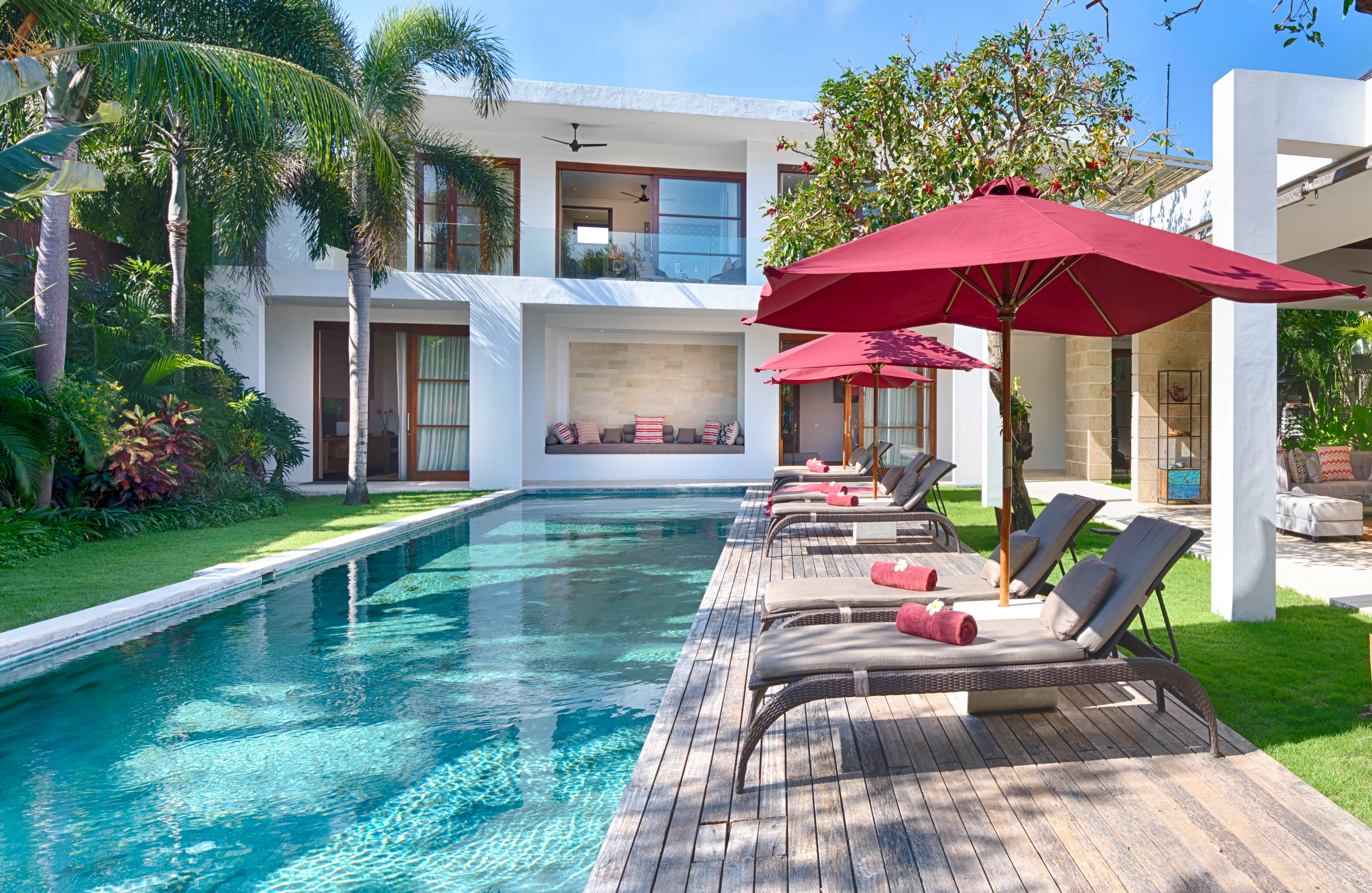 The length of the pool at Casa Brio from the shallow end, loungers under two claret parasols along the deck and the bedroom pavilion beyond